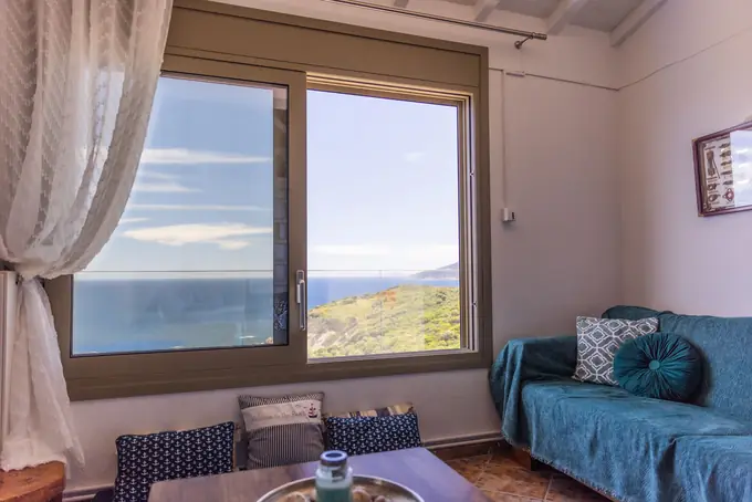 A sofa with teal throws beneath a sea-view window