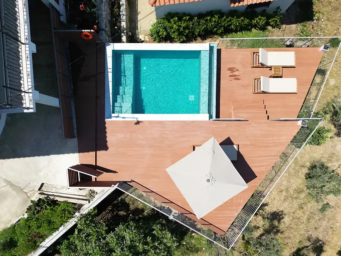 The pool and wooden deck with umbrella and sunbeds, from above