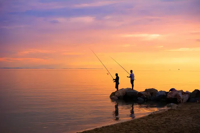 Two people fishing from the rocks at sunset