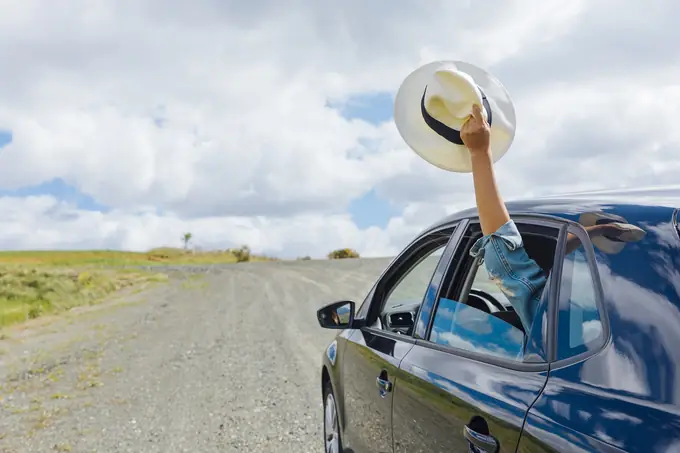 A hat waved from a car window on a country road