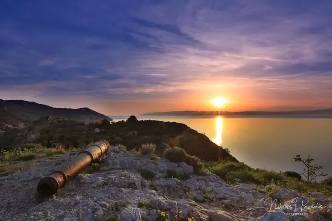 Sunset over the sea from the hillside, an old cannon in the foreground