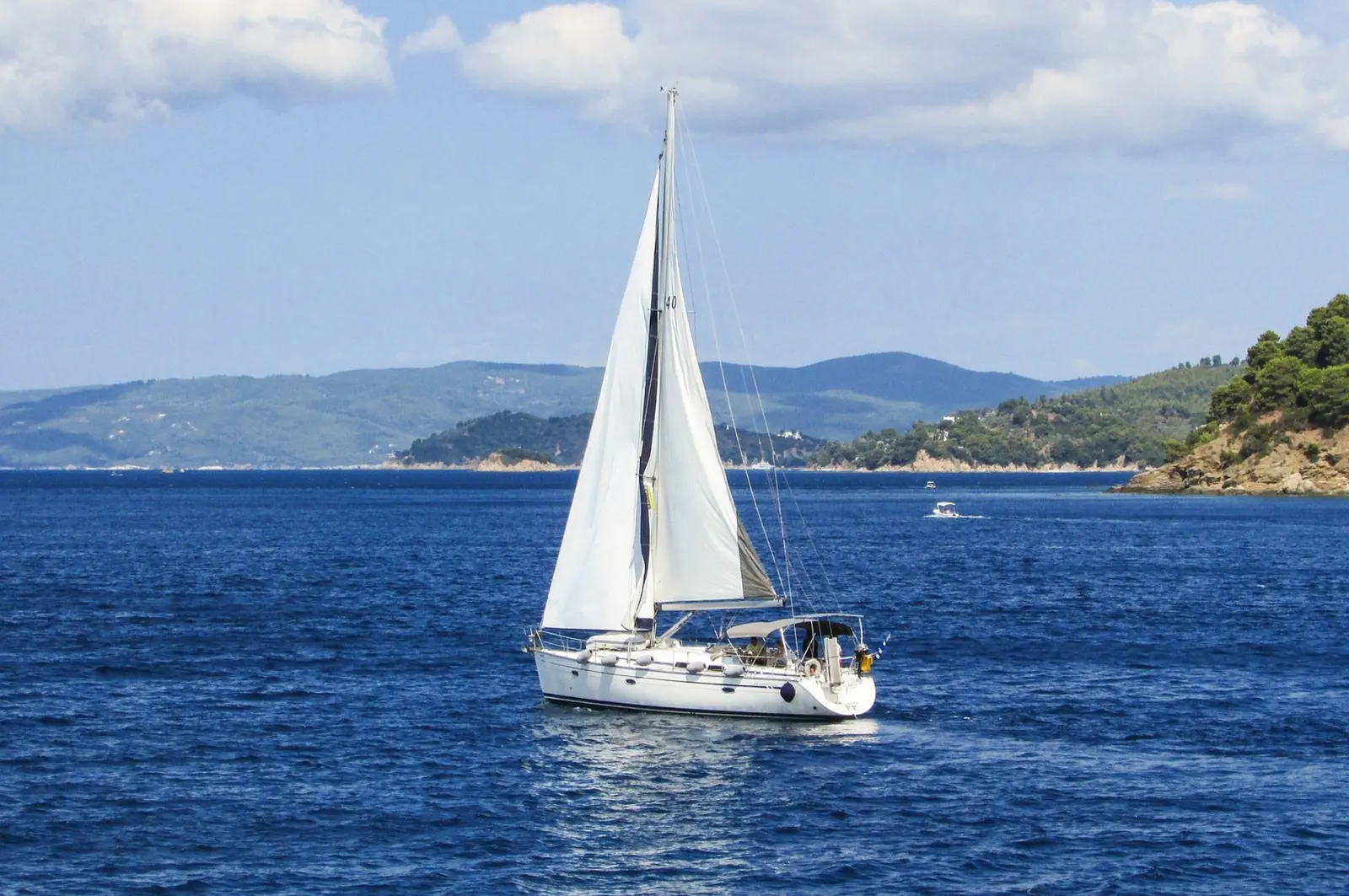 A sailing yacht off a green coastline